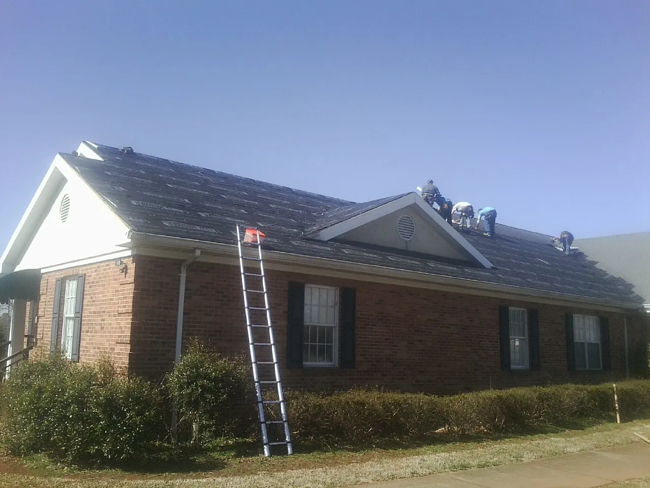 Crew tearing shingles off a brick ranch roof with a ladder set — Emergency Roof Repair work by our crew in Aroda