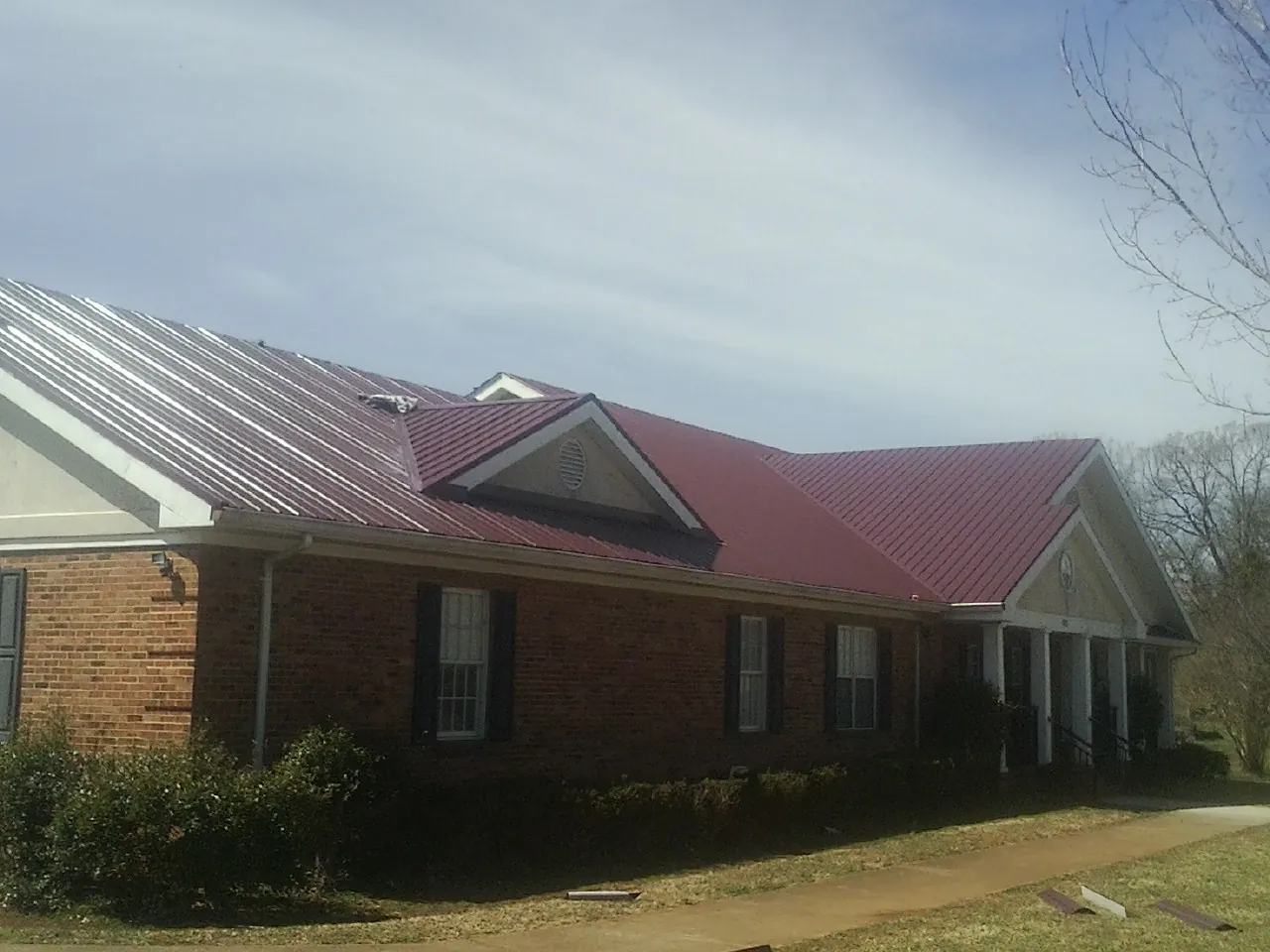 Red metal roof with gabled entries on a long brick building, from a Hail Damage Roof Repair job in Aroda