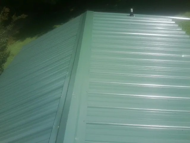 New green metal panels meeting at the ridge of a roof — Flat Roof Repair work by our crew in Aroda