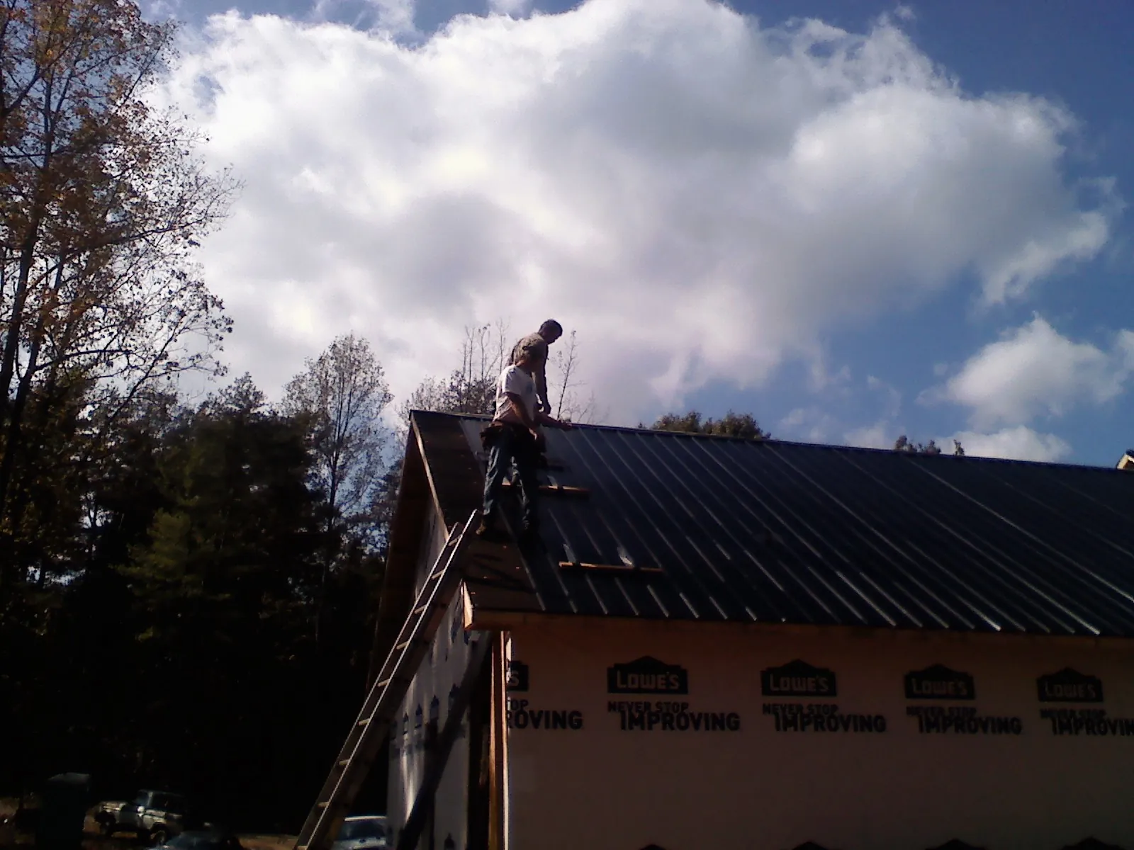 Roofer fastening dark metal panels high against a cloudy sky, from a Roof Inspection job in Aroda