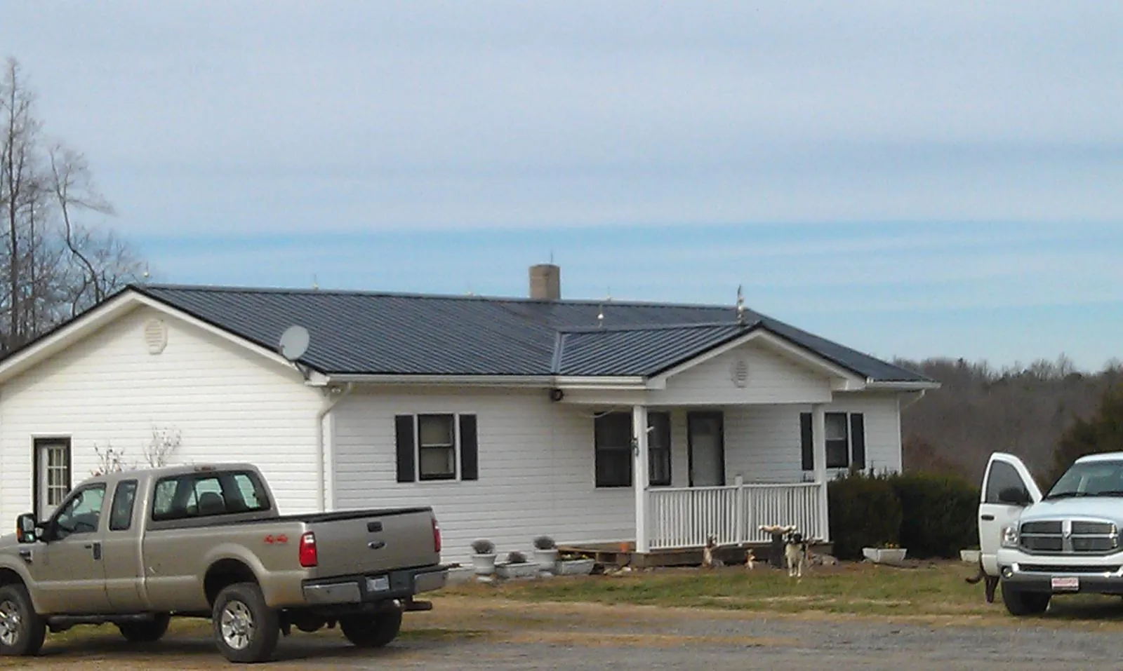 Finished dark metal roof on a white ranch home with work trucks parked in Aroda