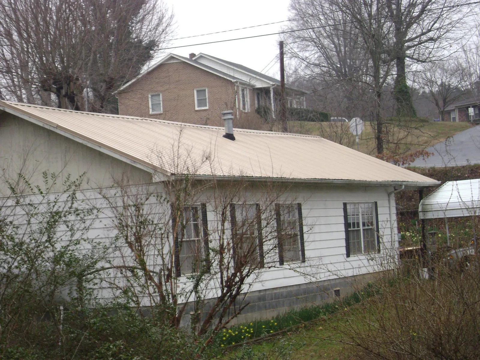 Tan metal roof on a white sided house set into a hillside — Commercial Roofing by Roofing Brothers in Aroda