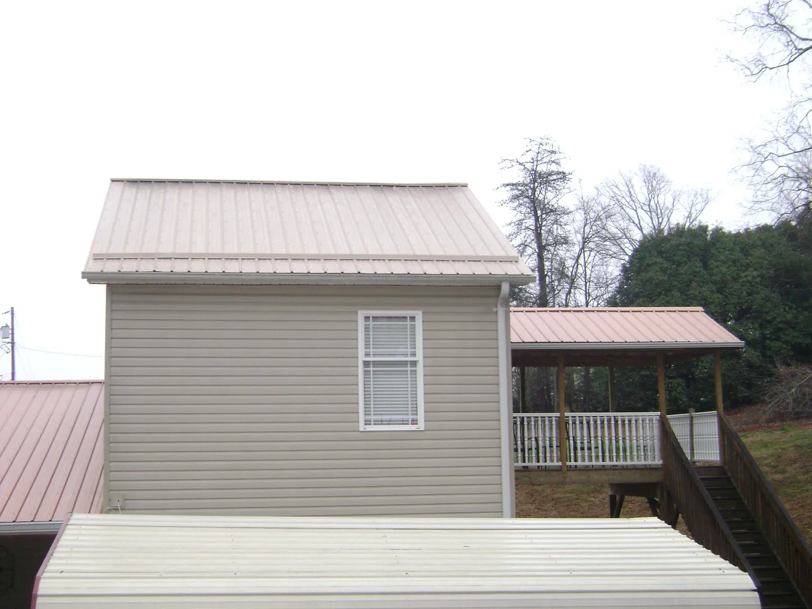 Tan metal roofs on a two story addition and attached porch, from a Roof Replacement job in Aroda
